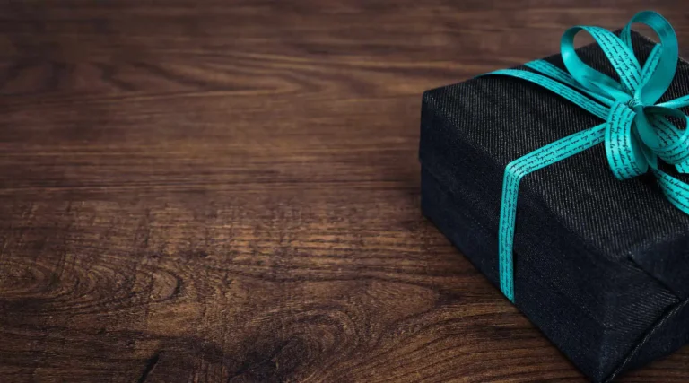 Nell'immagine, un pacchetto regalo con un fiocco azzurro poggiato su un tavolo in legno.