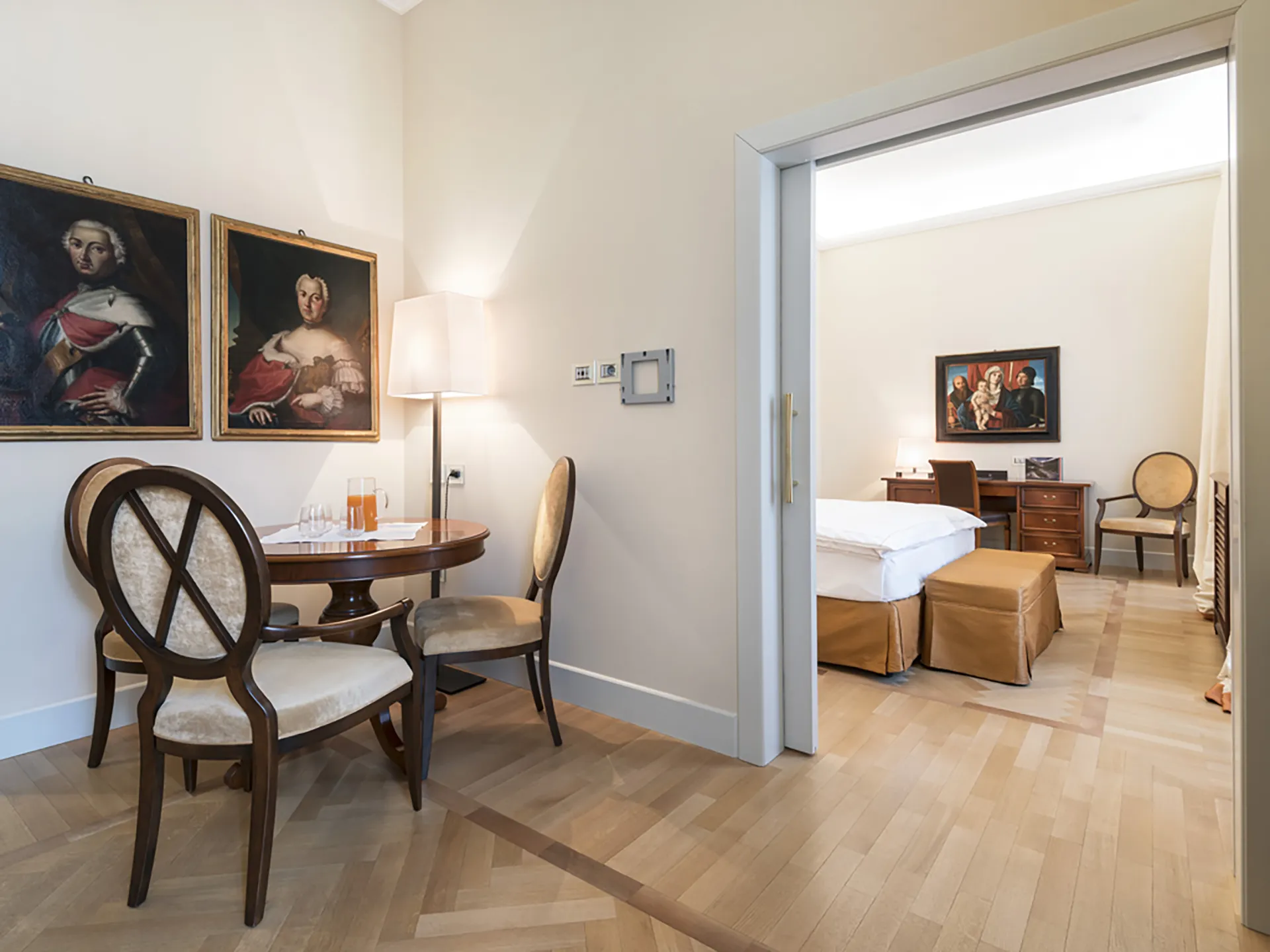 Nell'immagine, la zona giorno del Grand Hotel della Posta: si vede un tavolo tondo circondato da sedie, su cui sono poggiati una brocca di succo di frutta e dei bicchieri. Sulla destra, attraverso una porta scorrevole aperta, si intravede la camera da letto.