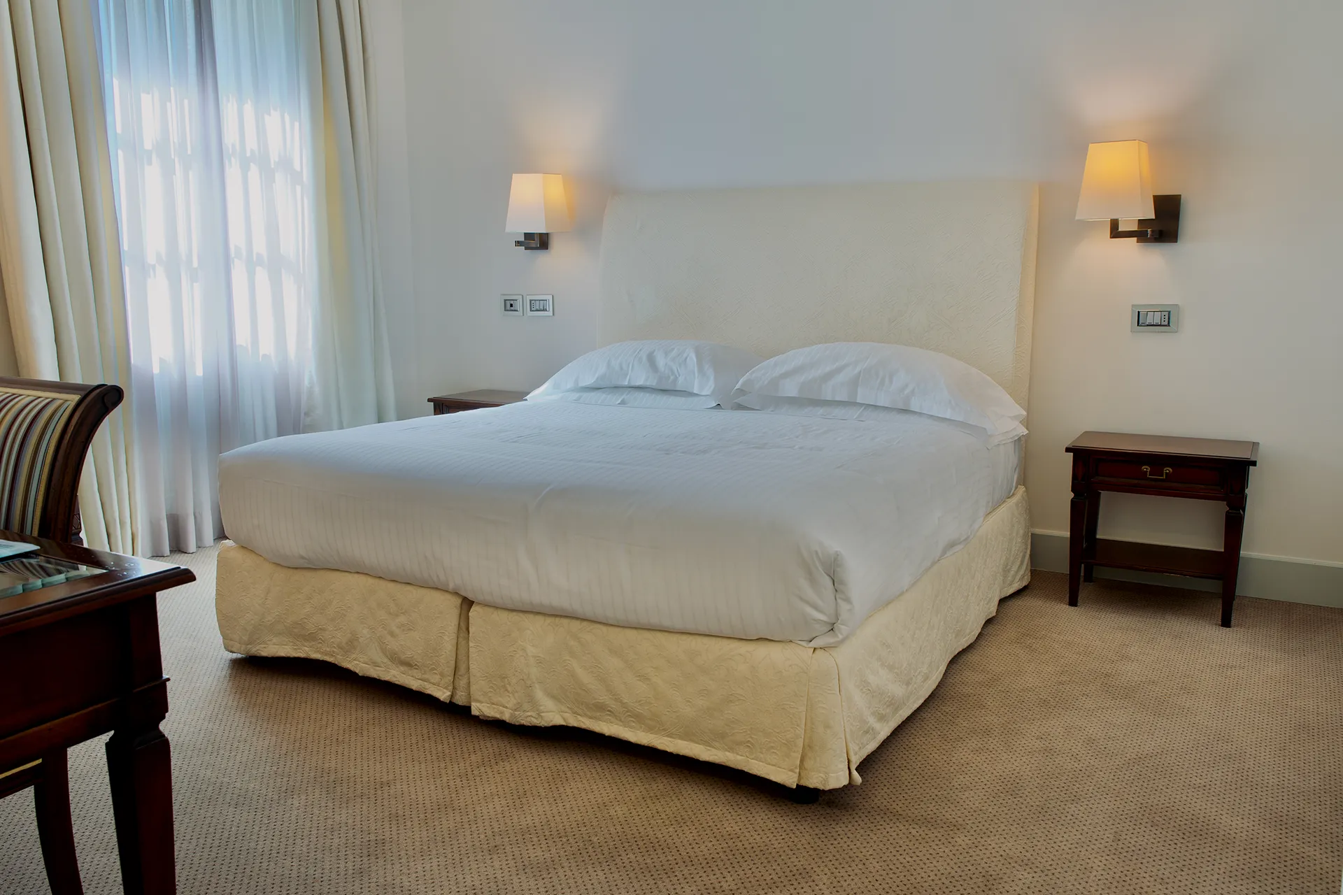 Nell'immagine, la camera Classic del Grand Hotel della Posta: si vede il letto matrimoniale e, di fronte, si intravede l'angolo di un tavolino con una sedia.