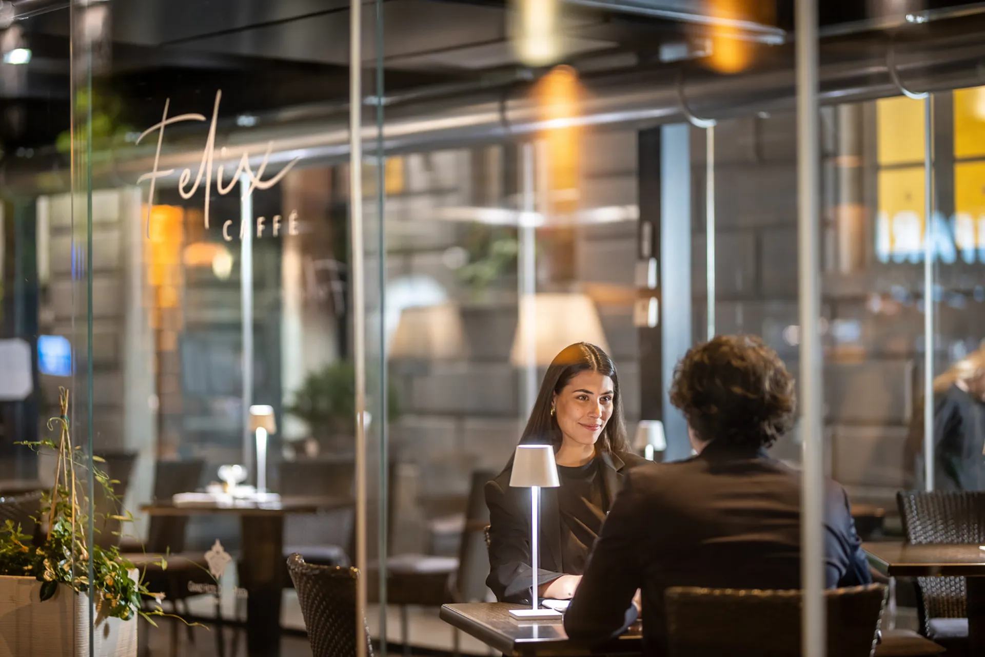 Nell'immagine, il dehor del bar del Grand Hotel della Posta: in primo piano, si vede una coppia di ragazzi seduti ad un tavolino. Sullo sfondo, una vetrata con l'insegna del bar.